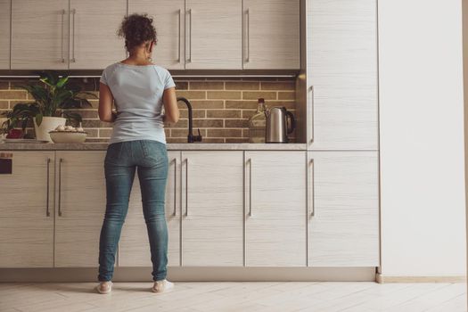 A woman stands with her back to the camera against the background of the kitchen near the sink