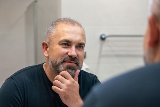 Middle-aged handsome man looking in mirror in bathroom