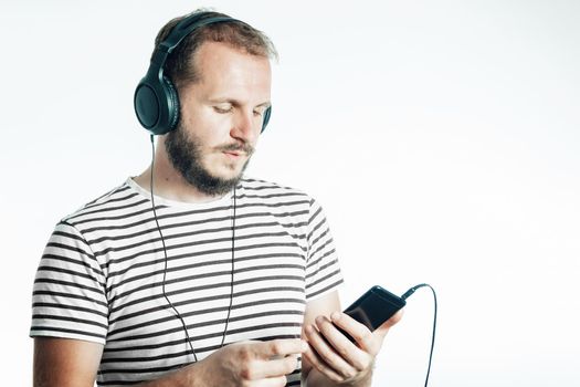 A bearded man listens to music on a smartphone with large headphones. 30-35 years old. Isolated on white.