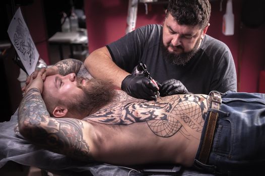 Tattooist demonstrates the process of getting tattoo in tattoo parlor