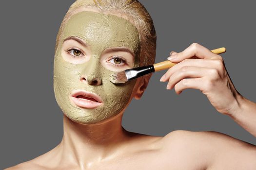 Beautiful Woman Applying Green Facial Mask. Beauty Treatments. Spa Girl Apply Clay Facial mask on grey background