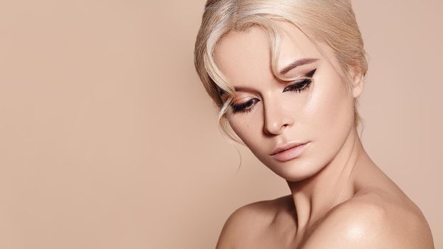 Sexy model with retro make-up, clean skin, blond hair on beige background. Elegant woman with fashion makeup, hairstyle
