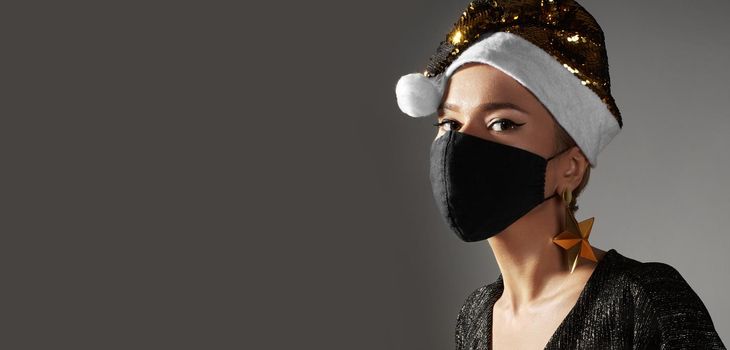 Woman with gold christmas hat, black medical mask. Fashion shiny style for xmas time. Protection from flu on holidays
