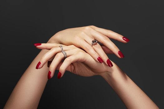 Elegant female hands with bright manicure. Square nails with red gel polish. Luxury fashion style of brilliants jewelry