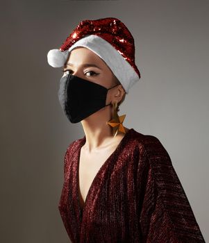 Woman with red christmas hat, black medical mask. Fashion shiny style for xmas time. Protection from flu on holidays