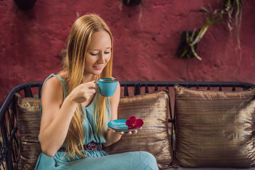 Young woman having a mediterranean breakfast seated at sofa and drinks hot aromatic coffee