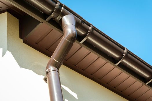 Brown pvc gutter connected to downpipe on roof edge.