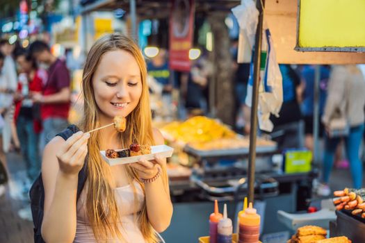 Young woman tourist eating Typical Korean street food on a walking street of Seoul. Spicy fast food simply found at local Korean martket, Soul Korea
