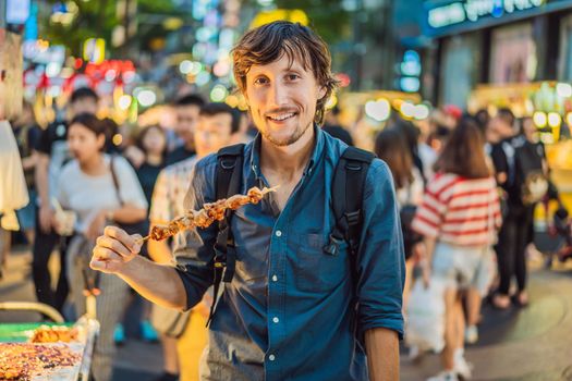 Young man tourist eating Typical Korean street food on a walking street of Seoul. Spicy fast food simply found at local Korean martket, Soul Korea