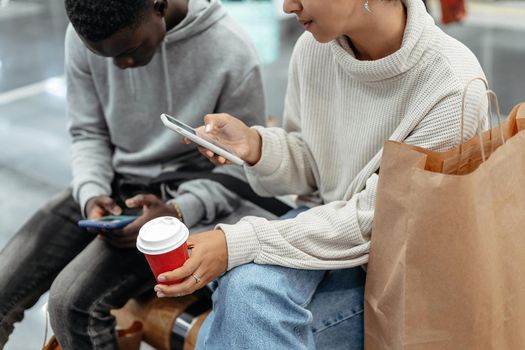 young people with smartphones and takeaway coffee sitting on a b
