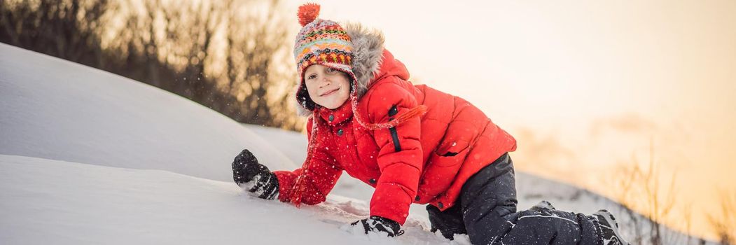 Boy in red fashion clothes playing outdoors. Active leisure with children in winter on cold days. Boy having fun with first snow. Happy little kid is playing in snow, good winter weather BANNER, LONG FORMAT