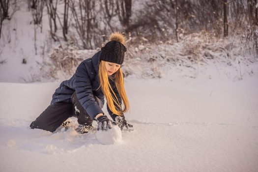 Young woman rolling giant snowball to make snowman