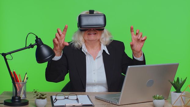 Senior businesswoman using headset helmet app to play simulation game watching virtual reality video