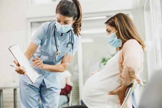 Worried Pregnant Woman With Protective Mask Talking To Nurse
