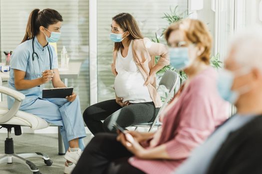 Pregnant Woman With Protective Mask Talking To Nurse At Waiting Room