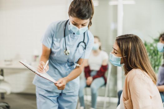 Woman With Protective Mask Talking To Nurse At Waiting Room