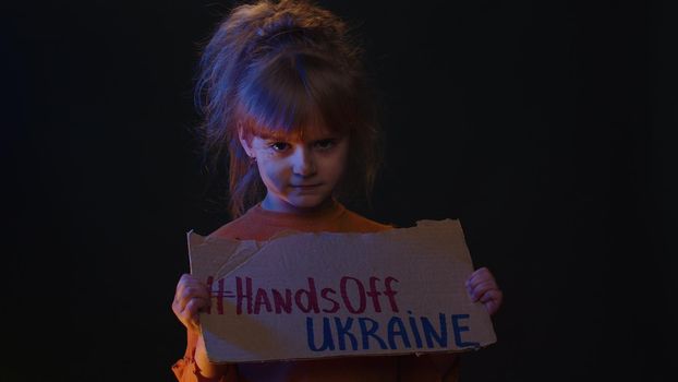 Upset homeless girl kid protesting war conflict raises banner with inscription Hands Off Ukraine