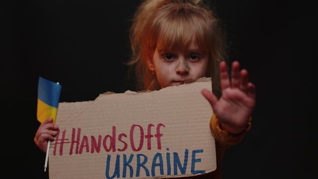 Scared poor girl homeless protesting war conflict raises banner with inscription Hands Off Ukraine