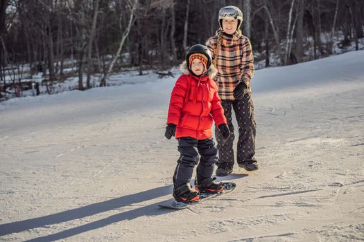 Mother teaches son snowboarding. Activities for children in winter. Children's winter sport. Lifestyle