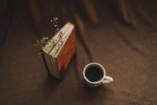A book with flowers and cup of coffee on dark background top view