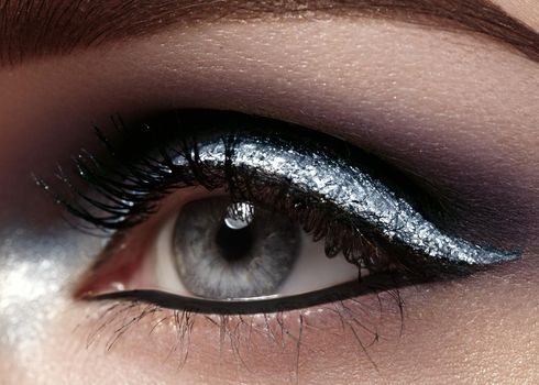 Beautiful macro shot of female eye with ceremonial makeup. Perfect shape of eyebrows, eyeliner and silver line on eyelid