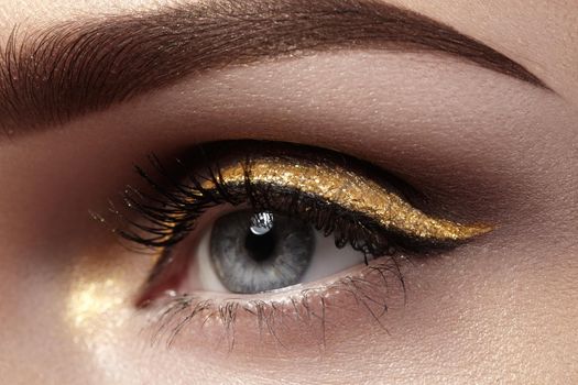 Beautiful macro shot of female eye with ceremonial makeup. Perfect shape of eyebrows, eyeliner and gold line on eyelid