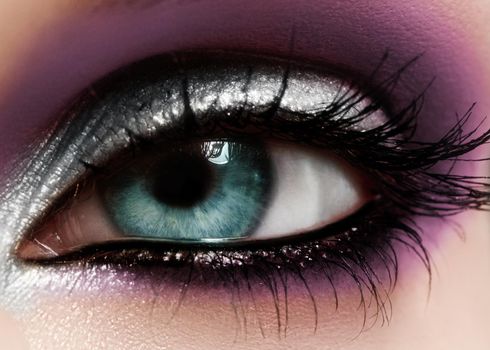 Closeup female eye with fashion bright make-up. Beautiful shiny silver, purple eyeshadow, wet glitter, black eyeliner