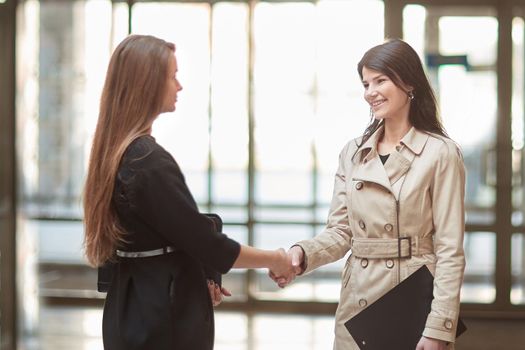 two businesswomen shaking hands in the office lobby.