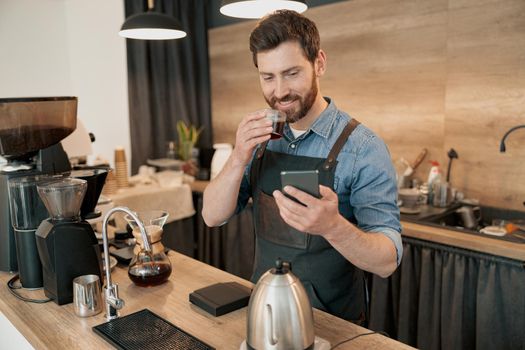 Handsome barista drinking coffee and scrolling through social media feed during lunch