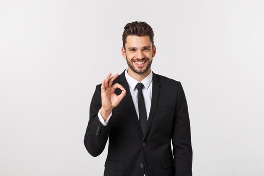 Handsome smiling businessman showing ok sign with fingers over gray background.