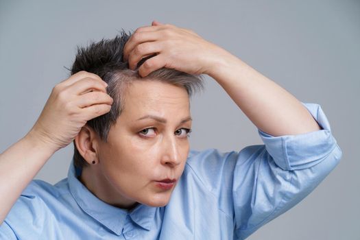 Portrait of mature woman in 50s checking her hair and unhappy to see a results in mirror. Beautiful grey haired woman dealing with dandruff problem checking in mirror