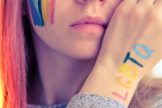 Rainbow LGBTQ flag painted on hand and cheek. Support for lgbt community. Honour of pride month. Connecting people, touching hands. Selective focus
