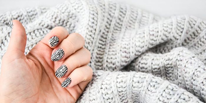 Hand in sweater with zebra animal printed nails. Female manicure. Glamorous beautiful manicure. Manicure salon concept