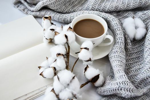 Cup of coffee with cotton plant notebook cinnamon sticks and anise star on white background. Sweater around. Winter morning routine. Coffee break. Copy space.