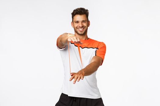 Charismatic male fitness instructor in activewear showing fitness exercises, teach clients how workout with resistance band, stretching with hands and smiling, training and active lifestyle concept