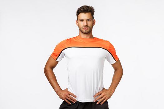 Manly, strong and confident sportsman, wear activewear, sports t-shirt, hold hands on waist, standing straight in assertive pose, fitness trainter look at clients workout, using gym equipment