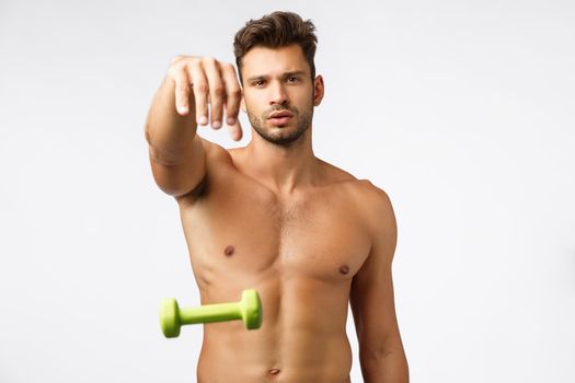Sport, wellbeing and masculinity concept. Sexy arrogant shirtless male athlete with perfect body, strong abdominal abs, good shape, standing naked torso drop green dumbell and looking sassy camera
