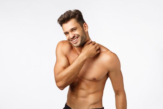 Sport, emotions and beauty concept. Handsome happy young sportsman with six-packs, touching neck and smiling camera with sexy expression, athlete posing naked torso, finish workout, white background