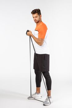 Strong masculine handsome sportsman in football activewear, standing full-length perform workout exercise with equipment. Serious good-looking athlete stand on resistance rope and stretch with hand