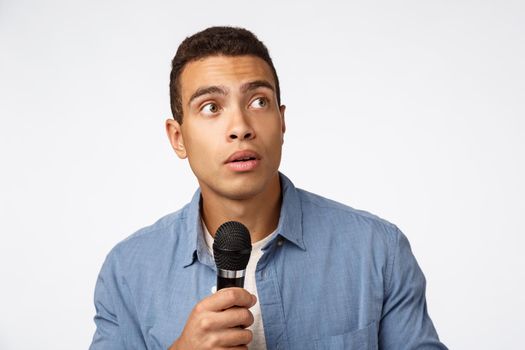 Surprised young man stop speech as hear strange noise, hold microphone, turn right and stare curious or intrigued, standing white background, prepare to sing on stage, worry perform in front audience