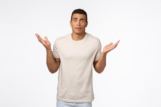Concerned and alarmed tanned muscline young man standing shocked and confused, shrugging with hands spread sideways, stare camera anxious and indecisive, have trouble dont know how solve situation