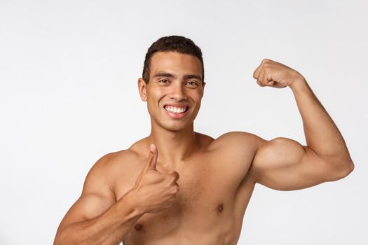 African American teenager shows muscles on arm. Isolated on white background. Studio portrait. Transitional age concept.