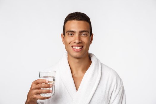 An attractive man drinking a glass of water against white background