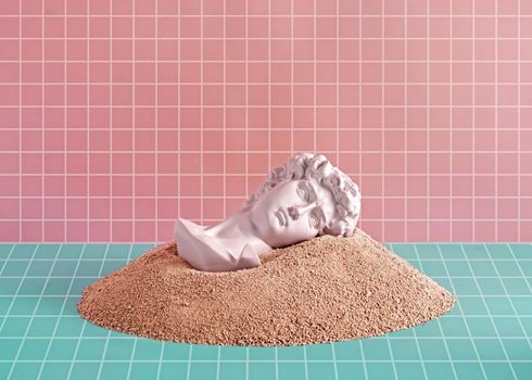 Sculpture of Michelangelo's David's head lies and dreams in the sand