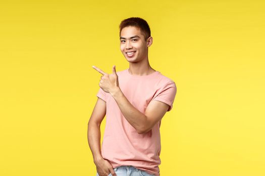 People, different emotions and lifestyle concept. Joyful handsome asian man pointing finger left, taiwanese guy introduce his project, showing way to shop or travel agency, smiling pleased