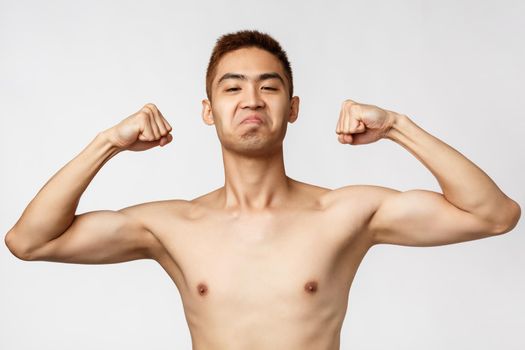 Workout, lifestyle and health concept. Portrait of confident and boastful handsome asian man standing naked torso, flex biceps, show-off his strength, exercising, standing white background