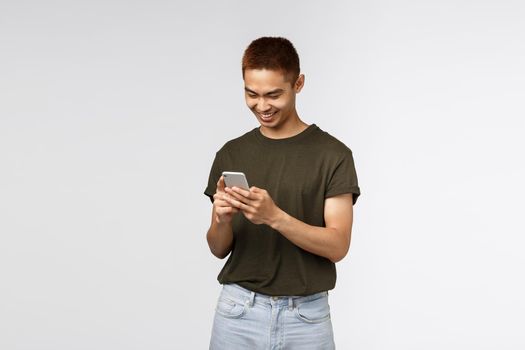 Technology, online lifestyle and communication concept. Cheerful handsome asian male student sending message, subscribe to internet language courses, using mobile phone, scroll news feed