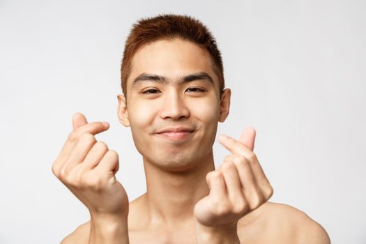 Beauty, skincare and men health concept. Close-up portrait of happy handsome asian naked man, showing korean love signs and smiling, express sympathy or like, white background
