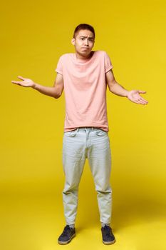 Lifestyle, education and people concept. Vertical shot of indecisive, puzzled asian teenage guy in stylish clothes, shrugging and spread hands sideways, look questioned, dont know, cant understand
