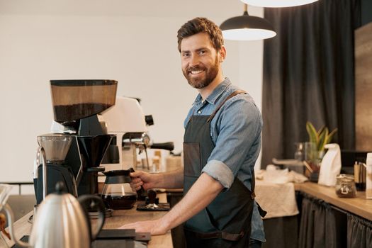 Smiling barista holding glass with filter coffee standing behind the counter